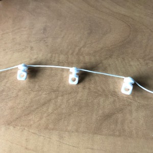 May include: White plastic curtain rings with a white string threaded through them.