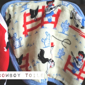 Puede incluir: Dos baberos para beb&eacute; con tem&aacute;tica de vaquero. Un babero es rojo con perros border collie negros y blancos. El otro babero es blanco con un borde azul y un patr&oacute;n de vaqueros, vaqueras, caballos, cactus y sillas de montar. El texto "COWBOY TOILE" est&aacute; impreso en la parte inferior de los baberos.