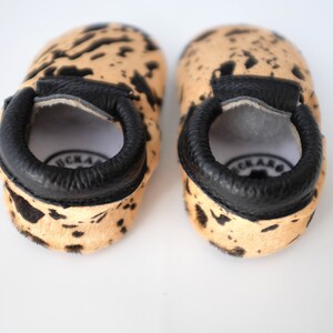 May include: A pair of brown and black cowhide baby moccasins with black leather trim. The moccasins have a soft, comfortable feel and are perfect for little feet.