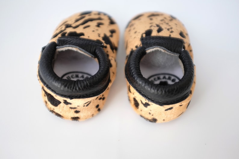 May include: A pair of brown and black cowhide baby moccasins with black leather trim. The moccasins have a soft, comfortable feel and are perfect for little feet.