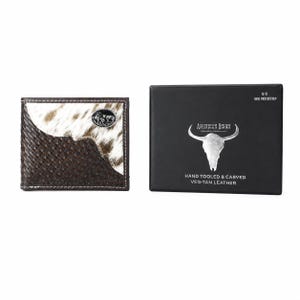 May include: A bi-fold wallet featuring a brown basket-weave leather base and a white and brown hair-on-hide panel with a silver bison emblem. Beside it is a black presentation box labeled American Bison Hand Tooled & Carved Veg-Tan Leather.