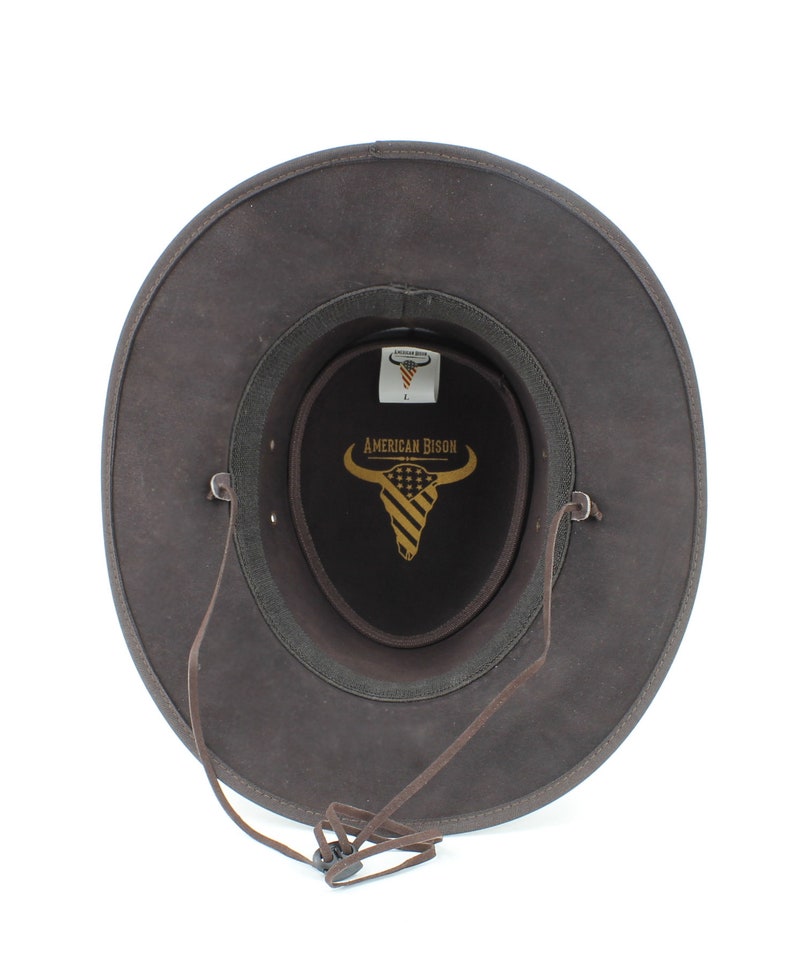 Pu&ograve; includere: Cappello da cowboy in pelle marrone con cinturino in pelle marrone e fibbia nera. Il cappello &egrave; foderato in feltro nero con un logo dorato che dice "American Bison" e una testa di bisonte stilizzata con un motivo a bandiera americana.