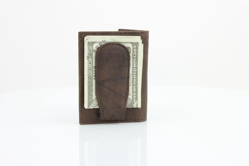 May include: A brown leather wallet with a money clip. The wallet has a fold-over design and is closed with a snap. The wallet is filled with cash.