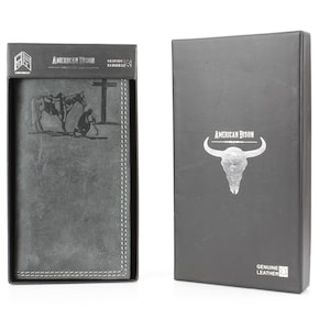 May include: A gray leather wallet with a detailed image of a cowboy and horse is displayed in its box. The box is black with the words "AMERICAN BISON" and "GENUINE LEATHER". The wallet is in a black box with the words "AMERICAN BISON" on the top.