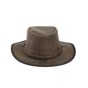 Pu&ograve; includere: Un cappello da cowboy in pelle marrone con una fascia in pelle intrecciata.