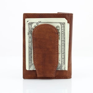 May include: A brown leather wallet with a money clip. The wallet has a billfold and a money clip to hold cash. The wallet is closed and a $100 bill is visible.