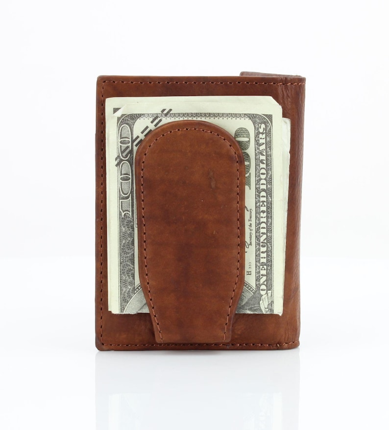 May include: A brown leather wallet with a money clip. The wallet has a billfold and a money clip to hold cash. The wallet is closed and a $100 bill is visible.