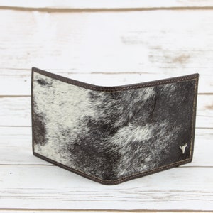 May include: A brown leather wallet with a white and black cowhide pattern. The wallet has a small silver bull's head logo on the front.