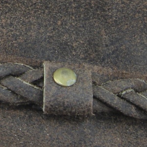 Pu&ograve; includere: Primo piano di un cappello di pelle marrone con una fascia in pelle intrecciata e un bottone in ottone.