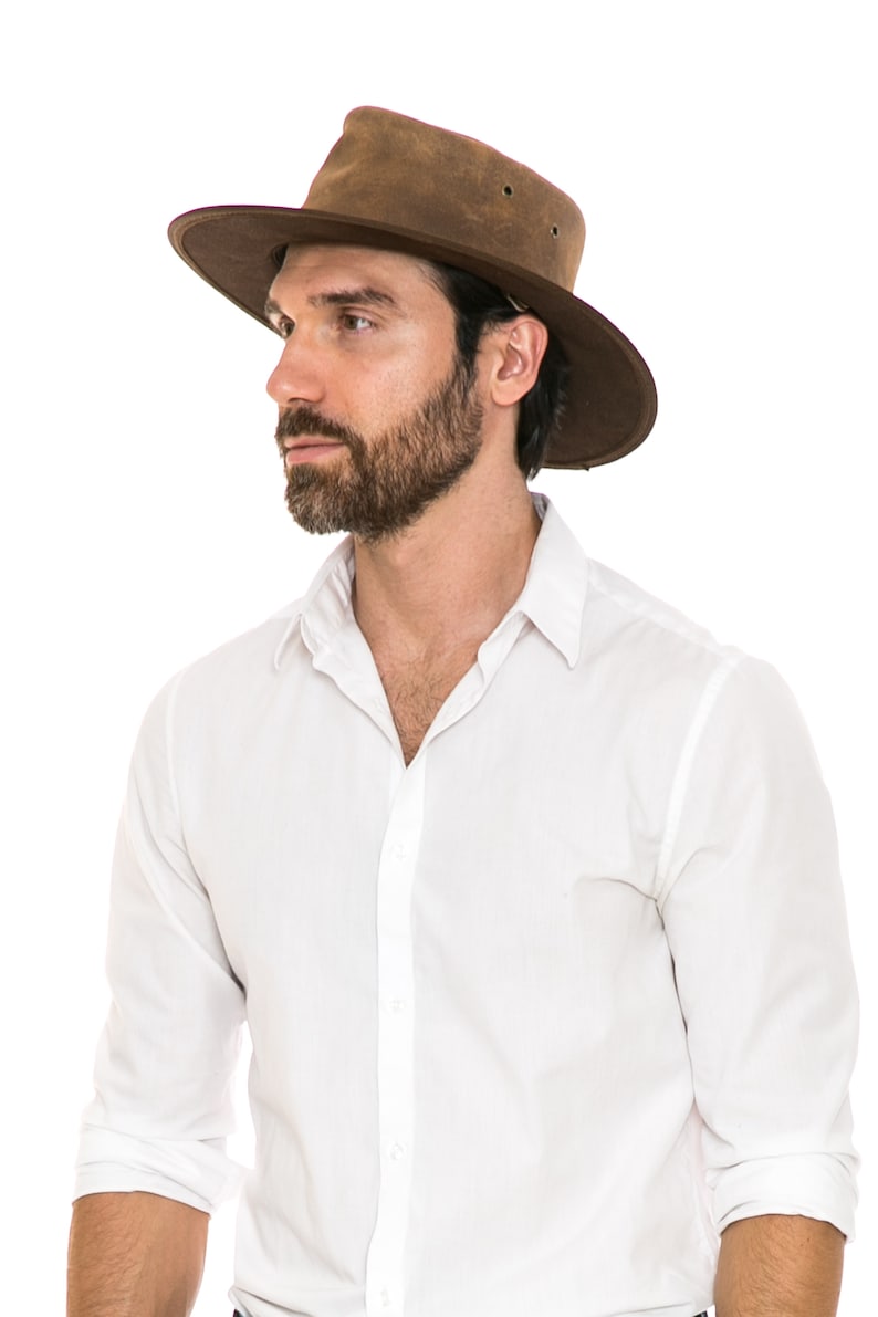 Pu&ograve; includere: Un uomo che indossa un cappello di pelle marrone a tesa larga e una camicia bianca abbottonata.