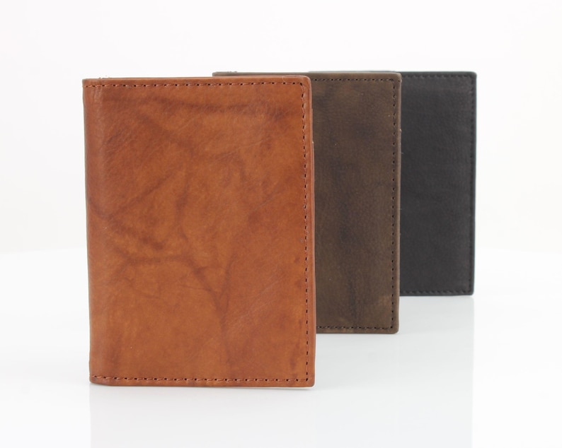 May include: Three leather wallets in different colors: brown, dark brown, and black. The wallets are lined up in a row, with the brown wallet in the front.