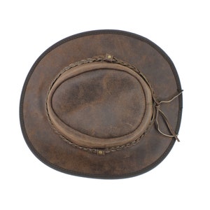 Pu&ograve; includere: Un cappello da cowboy in pelle marrone con una fascia intrecciata e una cravatta in pelle.