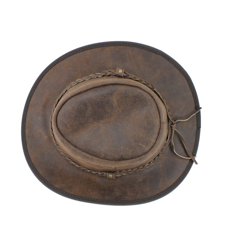 Pu&ograve; includere: Un cappello da cowboy in pelle marrone con una fascia intrecciata e una cravatta in pelle.
