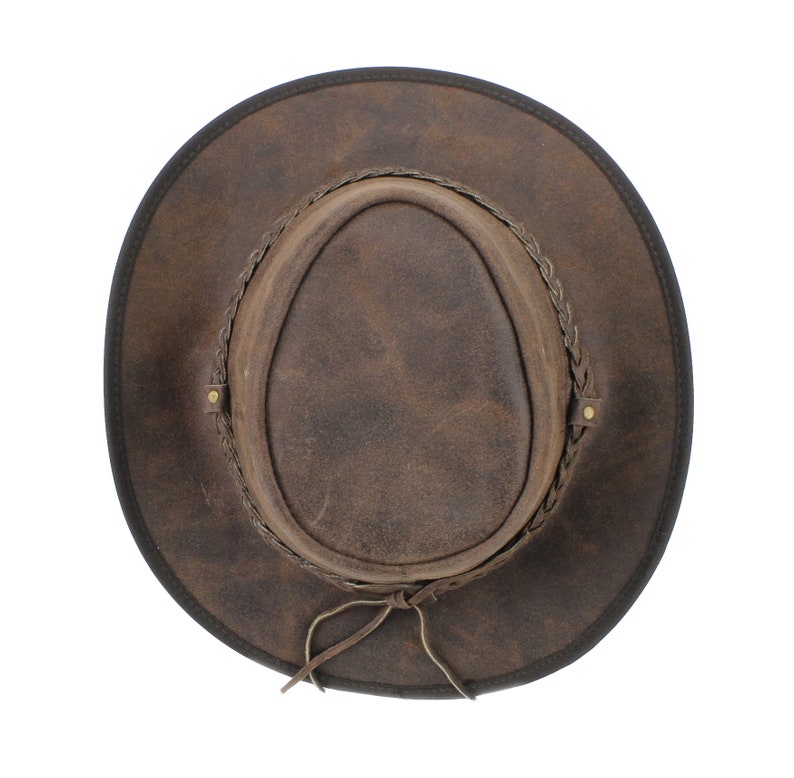 Pu&ograve; includere: Un cappello da cowboy in pelle marrone con una fascia in pelle intrecciata e un cinturino per il mento in pelle marrone.