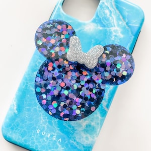 May include: A blue marble-patterned phone case with a glittery Minnie Mouse design. The Minnie Mouse design features three dark blue circles with iridescent glitter and a silver glitter bow. The phone case is a vibrant accessory.