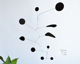 Peut inclure: Sculpture mobile noire et blanche avec des formes circulaires et en forme de larme suspendues à de fins fils. Le mobile est suspendu au plafond et est en mouvement. Le texte "Estudio del Arte" est visible dans le coin inférieur droit de l'image.