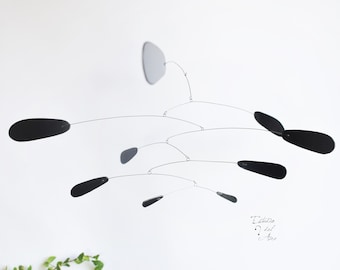 Peut inclure: Une sculpture mobile noire avec plusieurs pièces en forme de larme suspendues à de fins fils. Le mobile est suspendu au plafond.