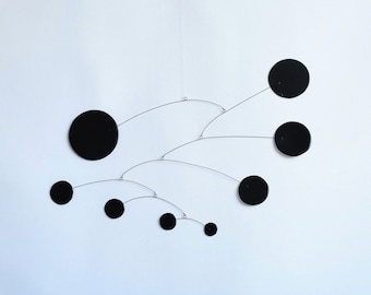 Peut inclure: Une sculpture mobile noire avec des formes circulaires suspendues à de fins fils. Le mobile est suspendu au plafond et est en métal.