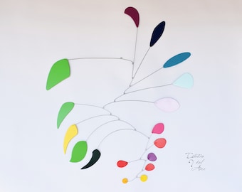 May include: A colorful mobile sculpture with various shapes and sizes of metal cutouts painted in different colors, including green, yellow, red, pink, blue, and purple. The mobile is suspended from the ceiling with thin wires.