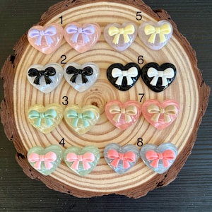May include: Eight pairs of heart-shaped resin embellishments with different colored bows. Each pair is numbered 1 through 8.