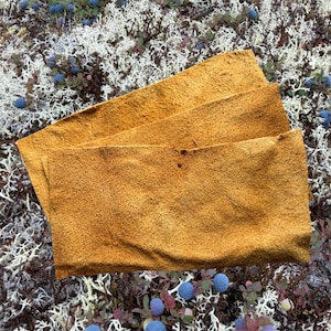 Puede incluir: Tres piezas rectangulares de cuero de ante color marrón dorado con un acabado mate y texturizado. Las piezas están superpuestas, mostrando una superficie suave y fibrosa con bordes irregulares que resaltan el grano natural del material.