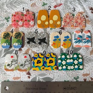 Op de afbeelding: Tien paar handgemaakte polymer clay oorbellen met verschillende ontwerpen. De oorbellen zijn in verschillende kleuren en patronen, waaronder bloemen, geometrische en abstracte ontwerpen. De oorbellen zijn allemaal rechthoekig of ovaal van vorm.
