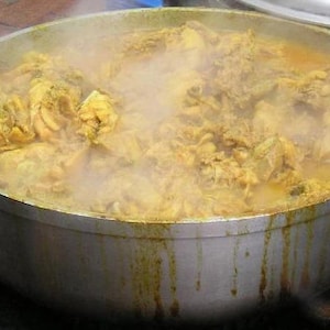 Puede incluir: Una olla grande llena de un curry amarillo humeante con pollo y verduras. La olla es de aluminio y tiene un asa a cada lado.