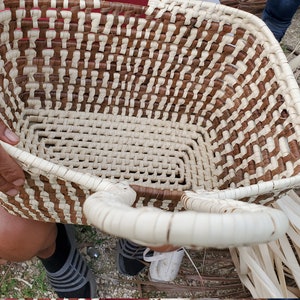 May include: A woven basket with a brown and white pattern. The basket has two handles and is being held by a person.