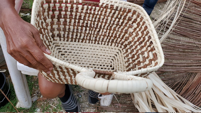 May include: A woven basket with a brown and white pattern. The basket has two handles and is being held by a person.