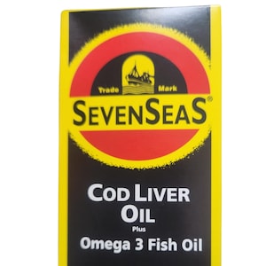 May include: A rectangular product box with a black background and bright yellow borders. The top features a red circle with a yellow sunburst effect, containing a black ship icon and the text Seven Seas. Below, the text reads Cod Liver Oil Plus Omega 3 Fish Oil in white.