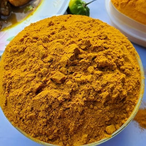May include: A close-up of a bowl filled with bright yellow turmeric powder. The powder is finely ground and has a smooth, even texture.
