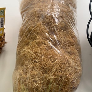 Puede incluir: Primer plano de una bolsa de fibra de coco seca de color marrón claro. La fibra está suelta y enredada, y está empaquetada en una bolsa de plástico transparente.