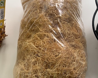 Puede incluir: Primer plano de una bolsa de fibra de coco seca de color marrón claro. La fibra está suelta y enredada, y está empaquetada en una bolsa de plástico transparente.