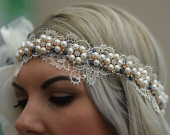 May include: A white lace headband with pearl and blue bead embellishments. The headband is worn by a person with blonde hair.