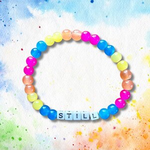 May include: A rainbow-coloured beaded bracelet with the word "STILL" spelled out in white letters.