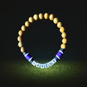 May include: A wooden bead bracelet with a purple, black, and white striped band spelling out "RAVENS".