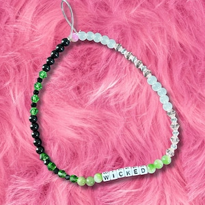 May include: A beaded phone charm with a variety of beads in black, green, clear, and light blue. The word "WICKED" is spelled out in white letter beads. The charm has a silver-colored loop at the top.