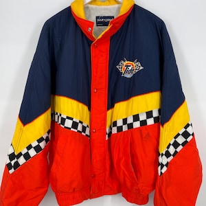 May include: A vintage racing jacket in navy blue, red, and yellow with a Tide logo. The jacket features a checkered pattern on the sleeves and a snap-button closure. The collar is yellow, and the jacket is hanging on a white hanger.