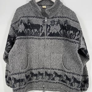 May include: Gray zip-up jacket with black horse and geometric pattern. The jacket has a high collar, two front pockets, and a drawstring at the bottom. The horse design is repeated around the jacket.