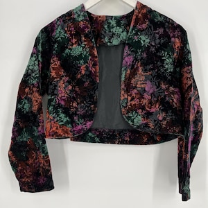 May include: A black velvet cropped jacket with a floral print in shades of orange, pink, and green. The jacket has long sleeves and a shawl collar.