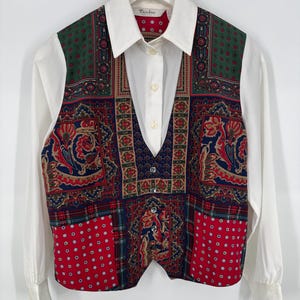May include: A vintage white collared shirt with long sleeves, paired with a patterned vest. The vest features a patchwork design in red, green, and navy blue with floral and paisley motifs. The vest has decorative buttons.