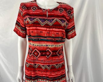 May include: A red, short-sleeved dress with a geometric pattern. The dress features a keyhole neckline and a repeating design of diamonds, triangles, and horizontal stripes in shades of red, pink, black, and teal. The dress is displayed on a mannequin.
