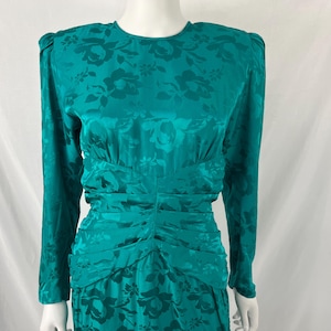 May include: Teal-colored vintage dress with a floral pattern. The dress features long sleeves, shoulder pads, and a ruched waist and skirt. The fabric has a subtle sheen, adding to its elegant appearance. A classic, formal dress.