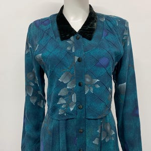 May include: Teal vintage dress with a black velvet collar and long sleeves. The dress features a button-down front and a pleated skirt. The fabric has a floral pattern in shades of gray and blue, with a quilted design.