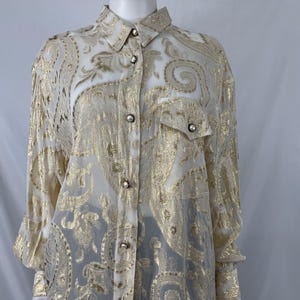 May include: A long-sleeved, sheer button-down shirt with a gold paisley pattern. The shirt has a collared neckline and a button-up front.