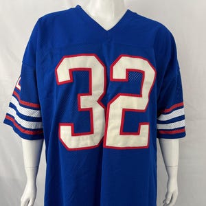 May include: A royal blue V-neck football jersey featuring the number 32 in large white numerals with red outlines on the chest. The short sleeves have white and red horizontal stripes, and the fabric has a visible mesh texture throughout.