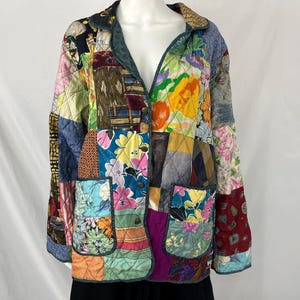 May include: A patchwork quilted jacket with a variety of floral and geometric patterns in shades of blue, green, pink, yellow, and red. The jacket has a button closure and two pockets.