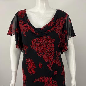 May include: Black dress with red paisley pattern. The dress features a cowl neckline and sheer, ruffled sleeves. The red pattern is distributed across the dress, with a concentration on the bodice and skirt.