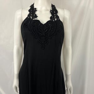 May include: Black halter dress with a decorative lace neckline. The dress is sleeveless and has a simple, elegant design. The lace detail adds a touch of sophistication to the overall look. The dress is displayed on a mannequin.
