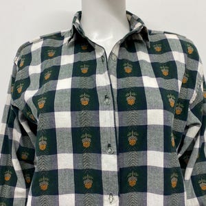 May include: Green, white, and navy blue plaid button-down shirt. The shirt features a repeating pattern of a gold-colored acorn design. The long-sleeved shirt is displayed on a mannequin.